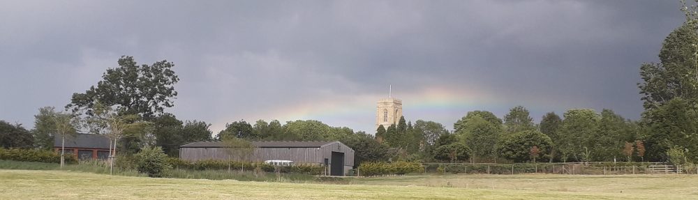 Photo of landscape and sky above St Peter's Church - In the sky is a rainbow arcing above the church