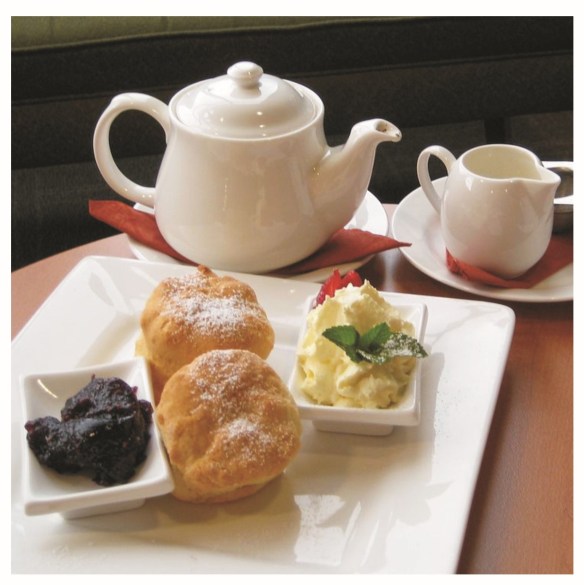 PHoto shows a white tea pot and milk jug with a plate of jam, scones and butter on a white tray