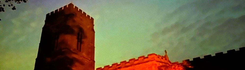 Photograph of St Peter's church at night with the colours of the Aurora Borealis in the sky above. The building looks orange with the subtle greens and pinks in the sky behind